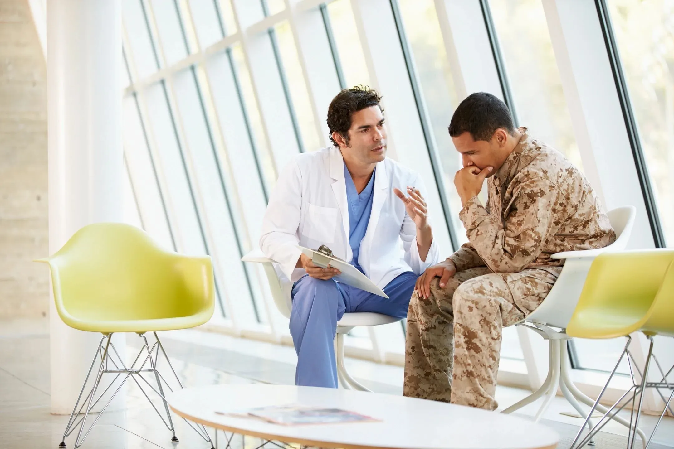 A service member talking with a clinician in a sunlit waiting room