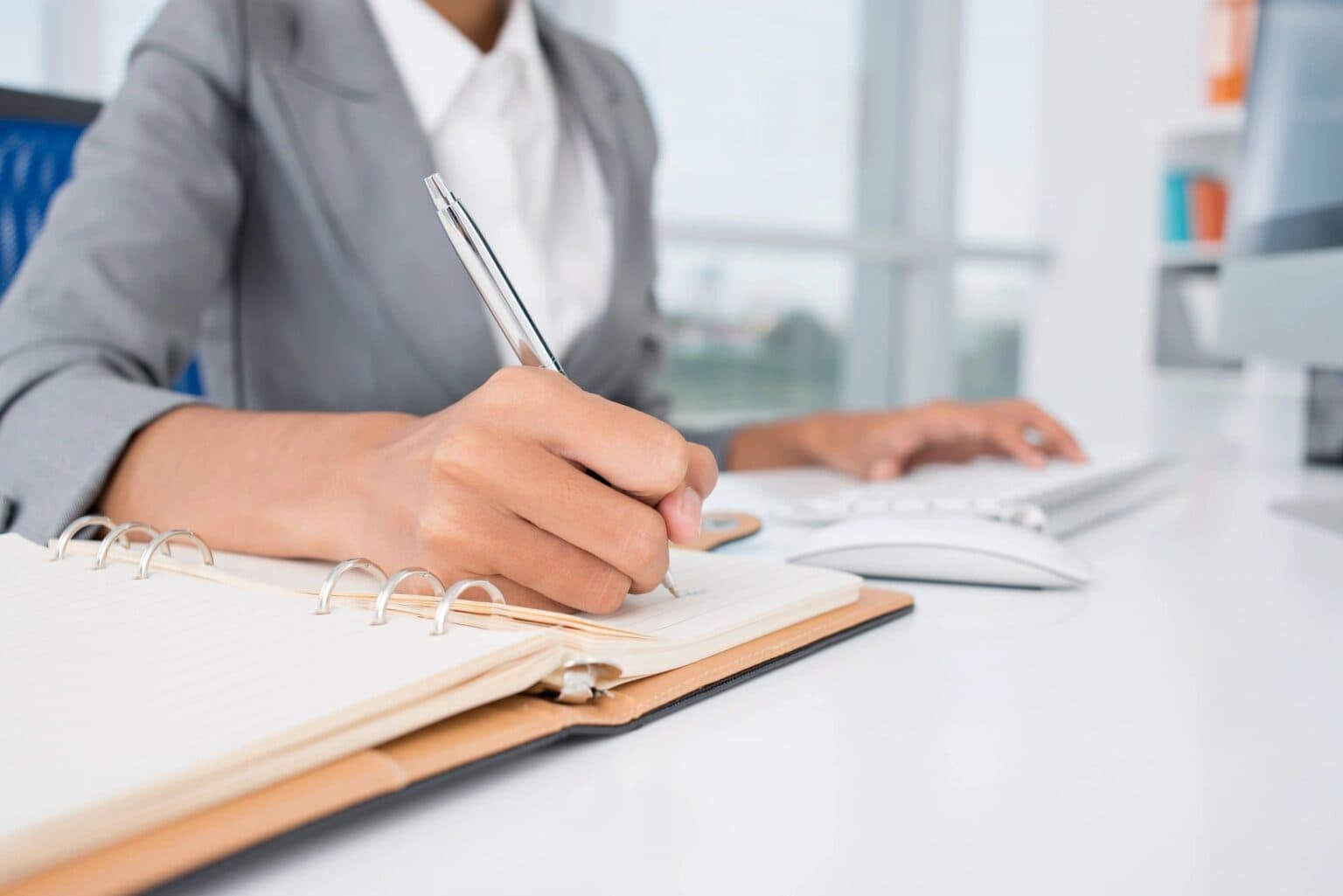 Hands writing in a notebook at a desk beside a keyboard