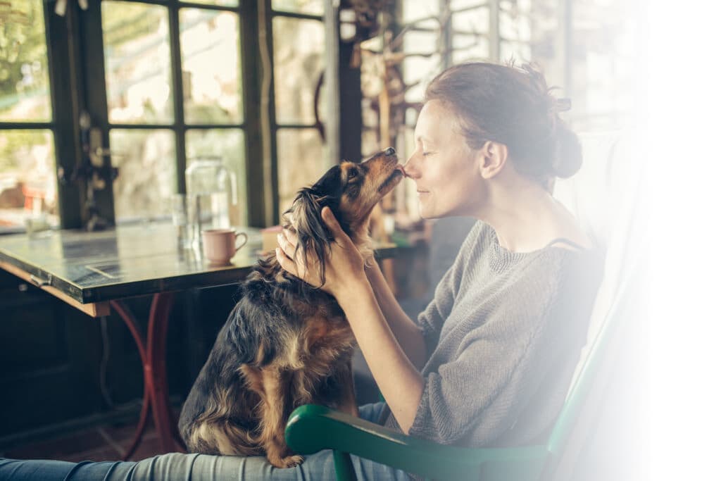 A woman at a kitchen table resting her forehead against her dog
