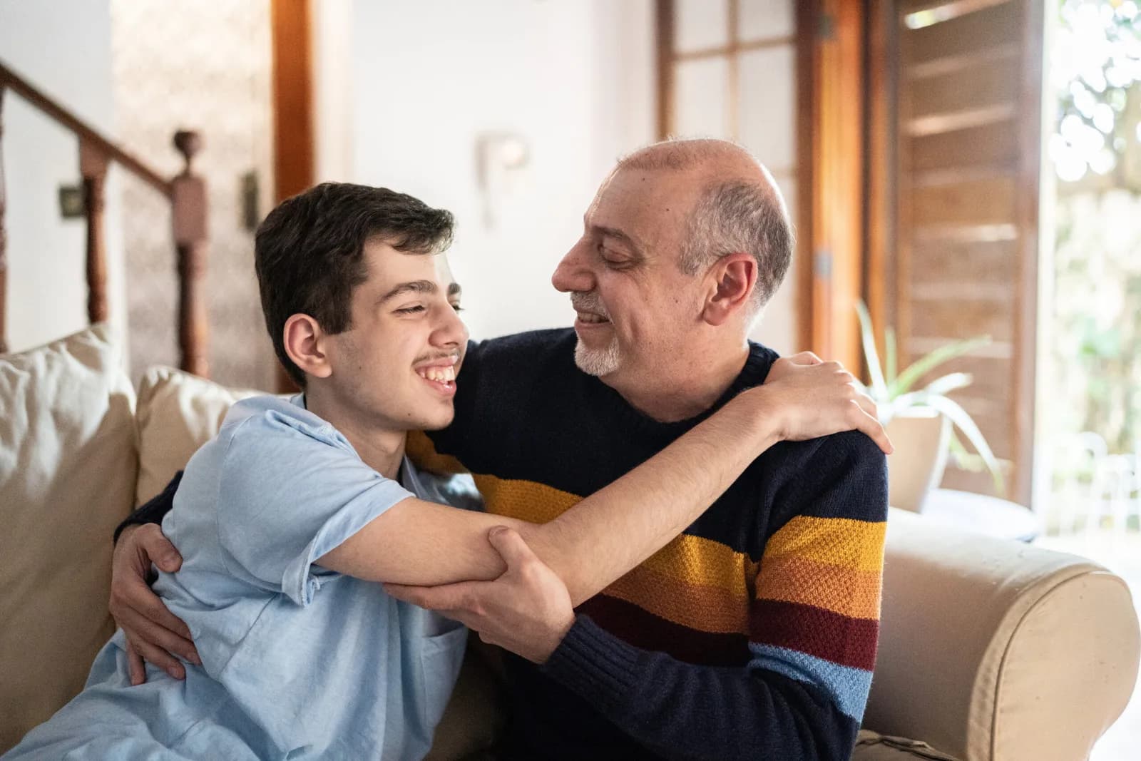 A father and teenage son laughing together on a couch at home.