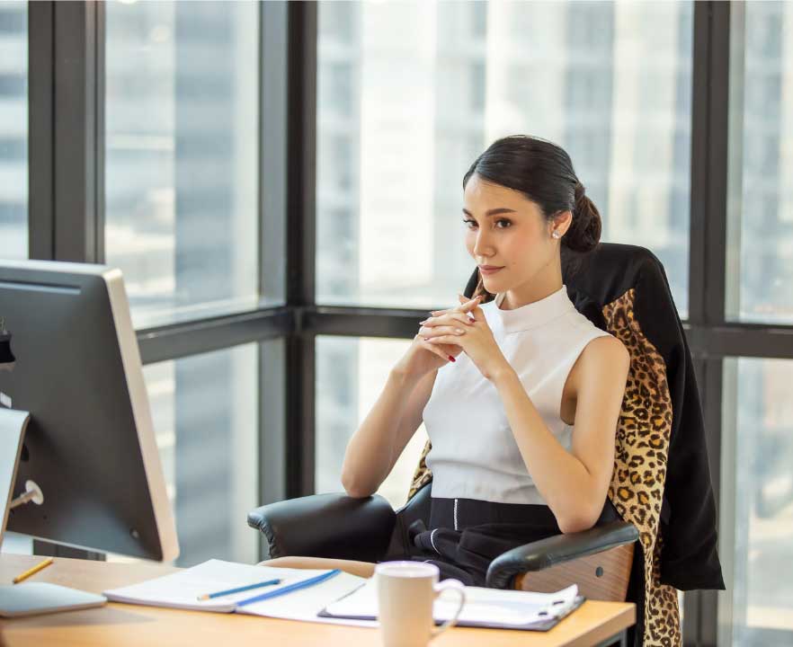 A woman seated at an office desk beside a computer monitor