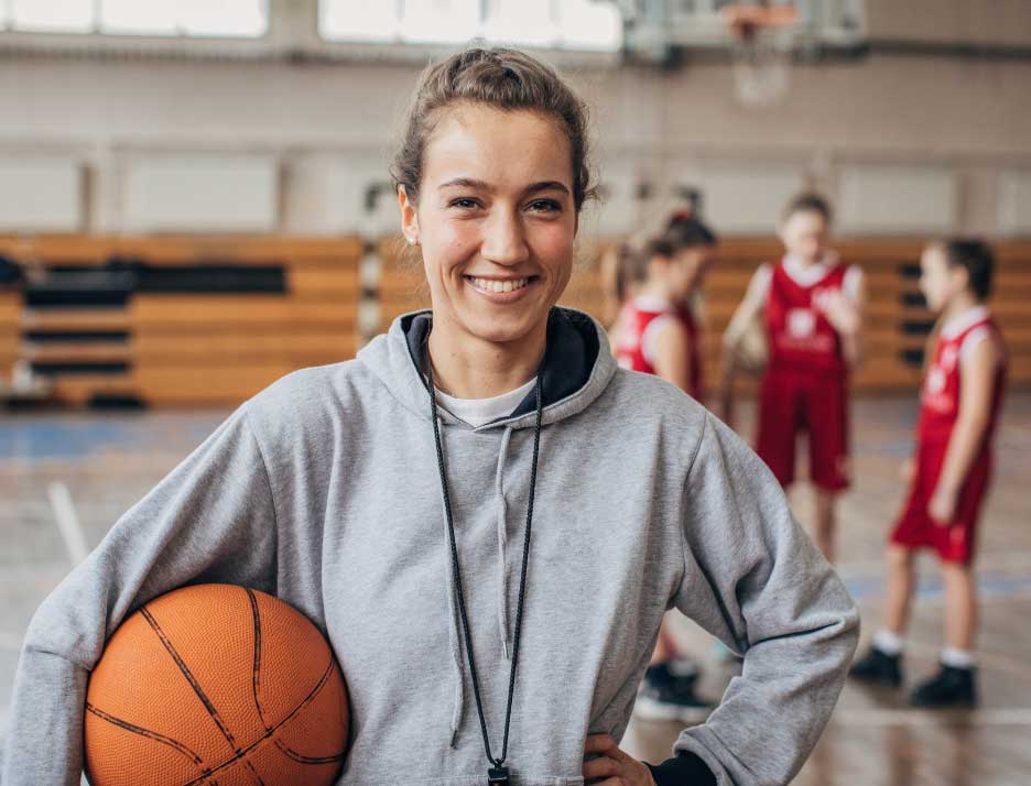 Coach holding a basketball with young athletes in the background