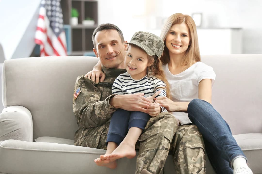 A uniformed father sitting on a couch with his daughter and her mother